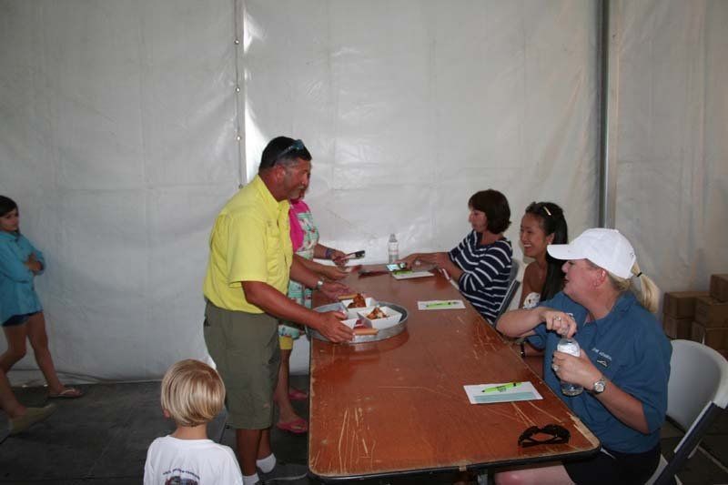 A man in a yellow shirt is serving food to a group of people sitting at a table