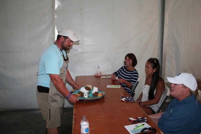 A man is serving food to a group of people sitting at a table.