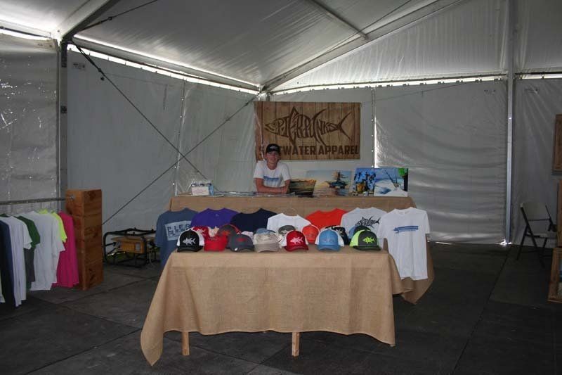 A man is standing behind a table with shirts and hats on it.