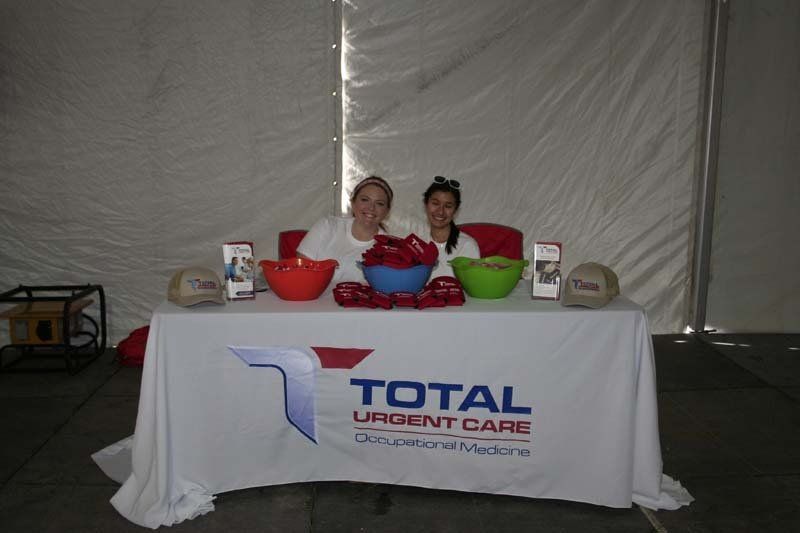 Two women sitting at a table with a sign that says total urgent care