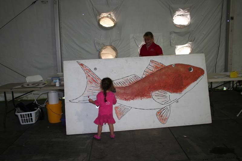 A little girl is standing in front of a large painting of a fish