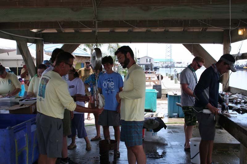 A group of people are standing around a table with one man wearing a blue shirt that says one