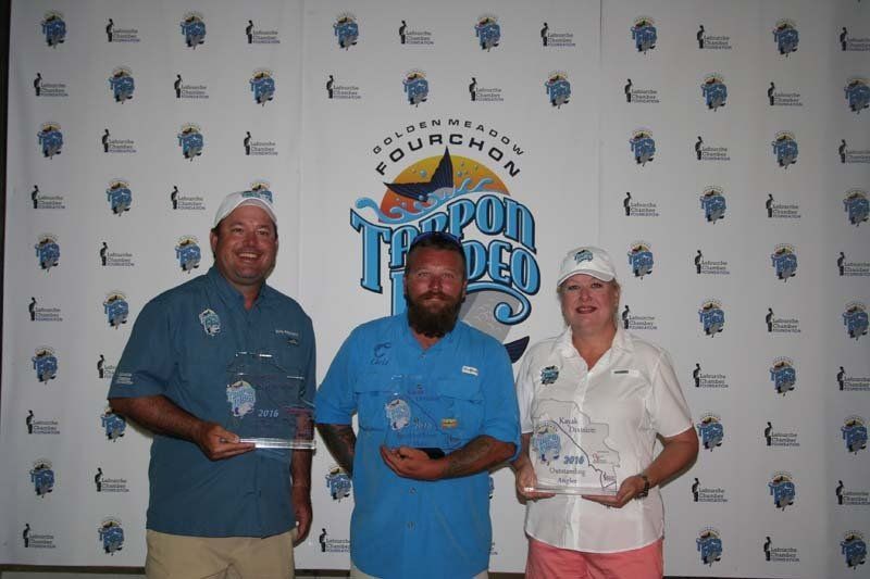 Three people are posing for a picture in front of a wall.