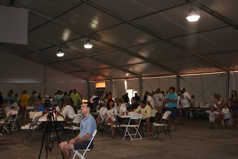 A man is sitting in a chair in a large tent surrounded by people.