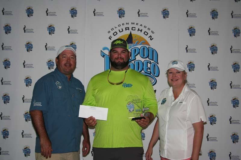 Two men and a woman are standing in front of a wall that says fourchon