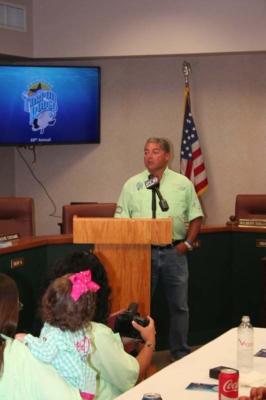 A man stands at a podium giving a speech in front of a screen that says texas road