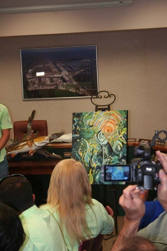 A group of people are sitting in front of a painting on an easel.