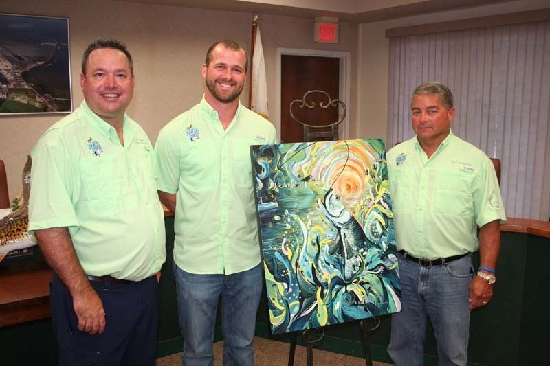 Three men are standing next to each other holding a painting.