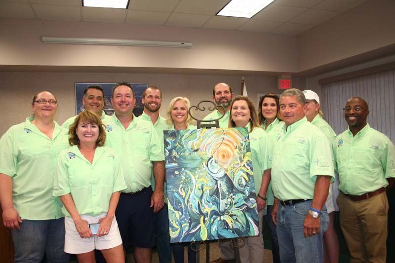 A group of people in green shirts are posing for a picture with a painting.