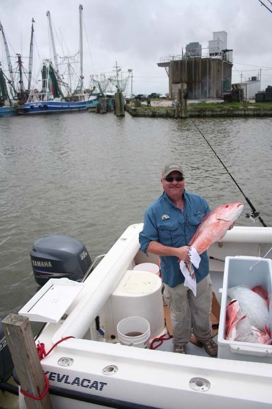 A man is standing on the deck of a boat holding a large fish.