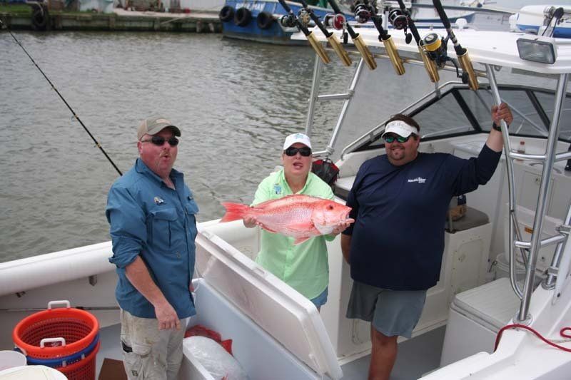 Three people on a boat holding a large red fish