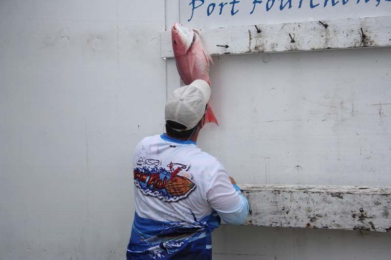 A man is holding a large fish in front of a sign that says port