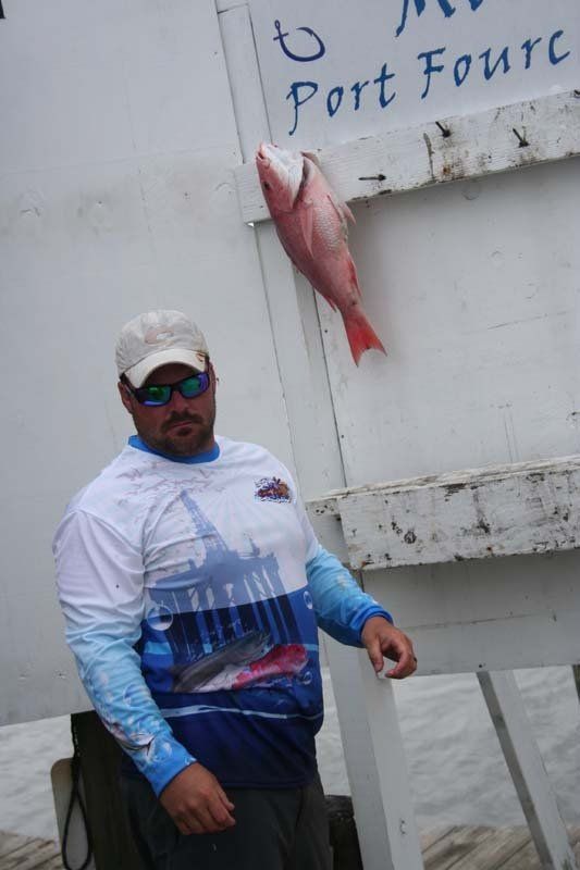 A man holding a fish in front of a sign that says port fourc