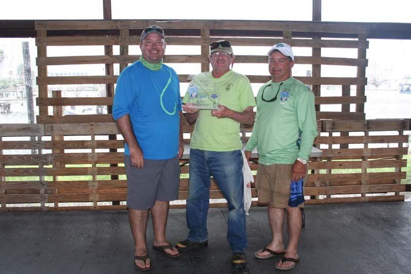 Three men are standing next to each other in front of a wooden wall.