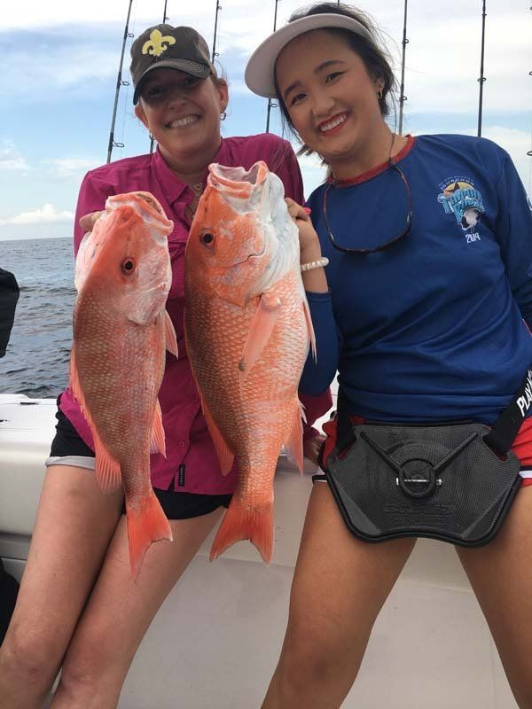 Two women are holding two red fish on a boat.