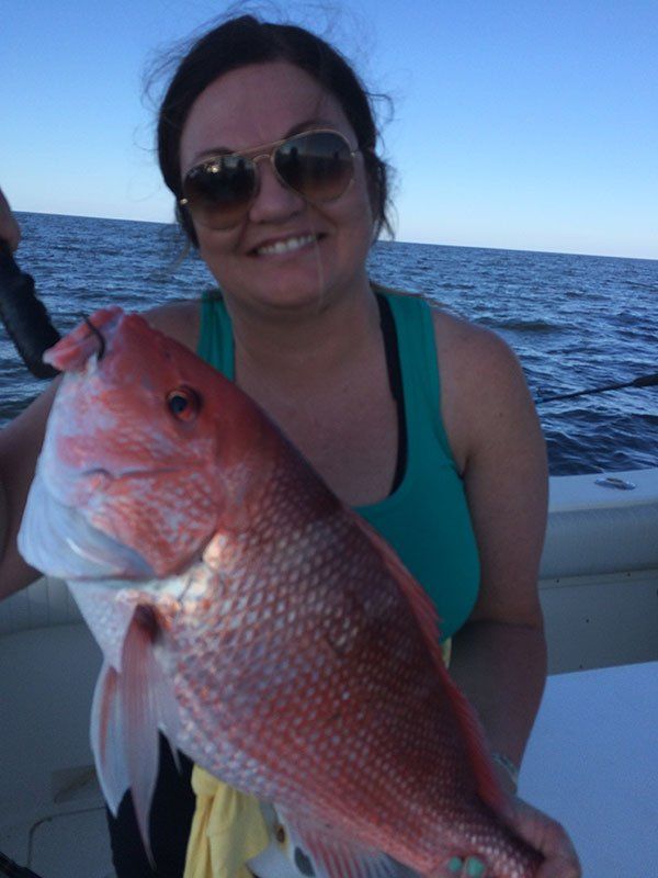 A woman is holding a large red fish on a boat
