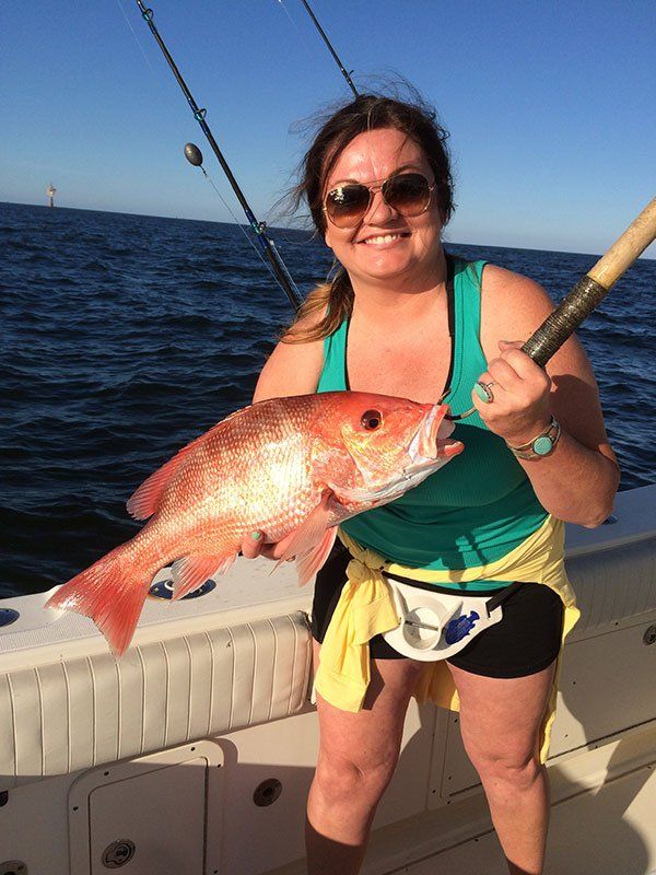 A woman is holding a large red fish on a boat.
