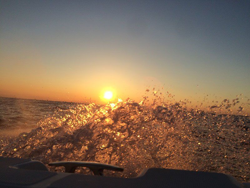 A boat is going through the ocean at sunset.