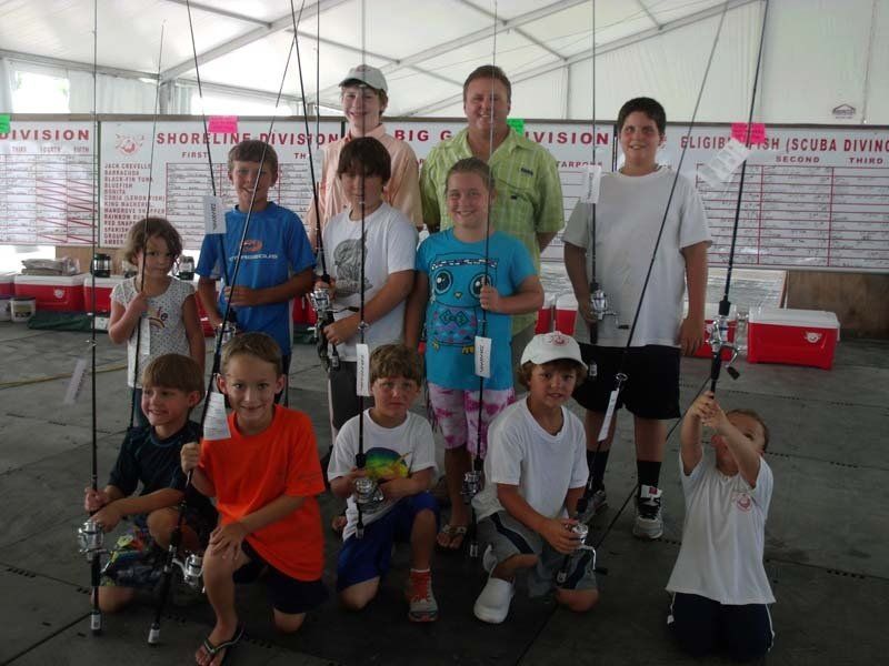 A group of kids holding fishing rods pose for a picture