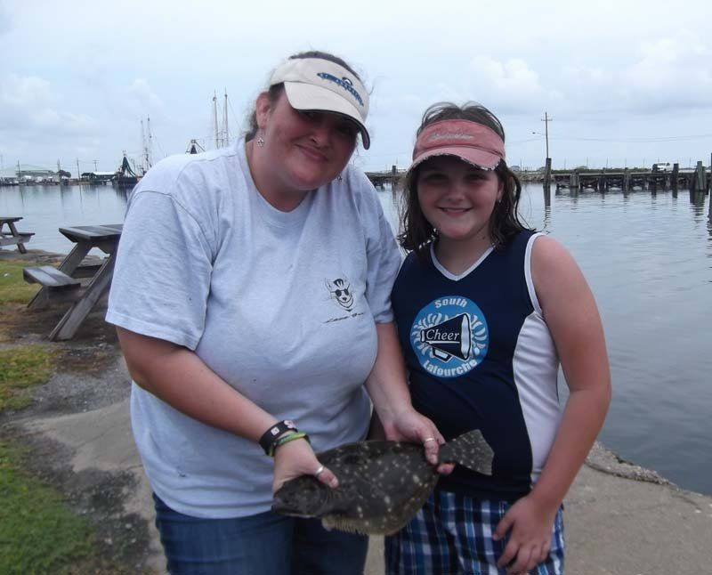 A woman and a girl holding a fish in front of a body of water