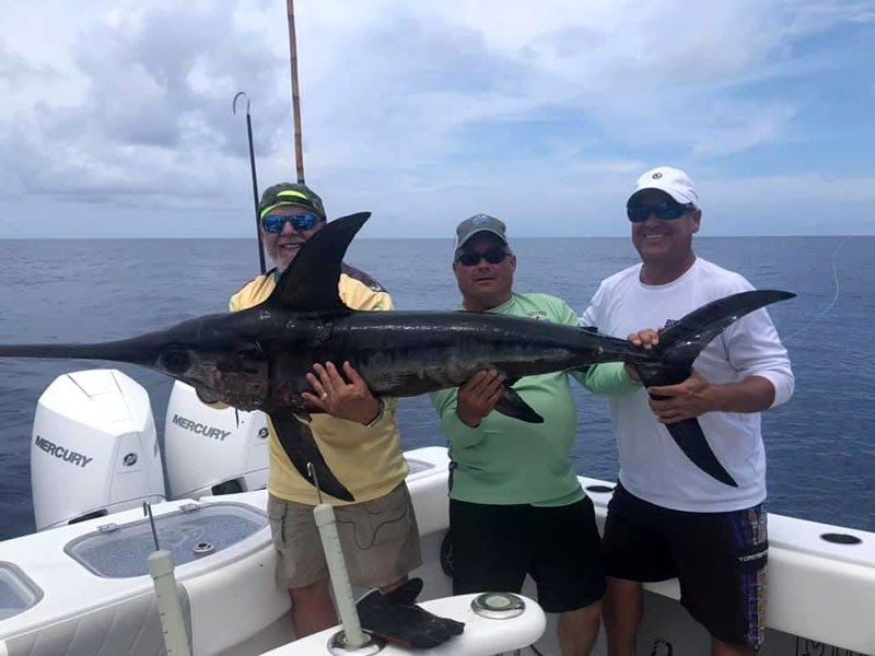 Three men are standing on a boat holding a large fish.