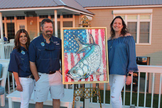 A group of people standing next to a painting of a fish on an easel.