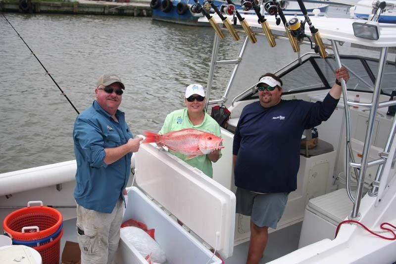 Three people on a boat holding a red fish
