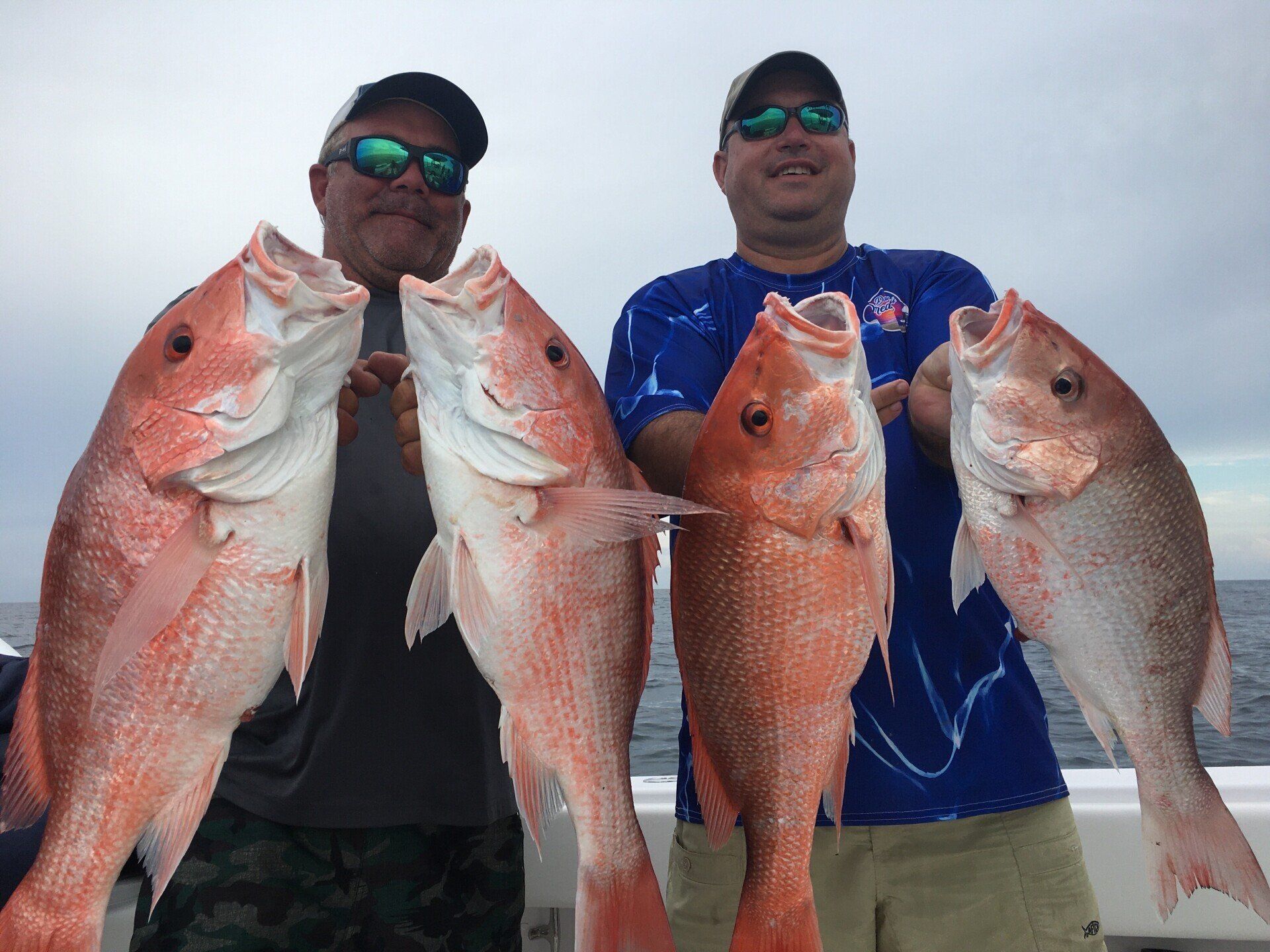 Two men are holding three large red fish on a boat.
