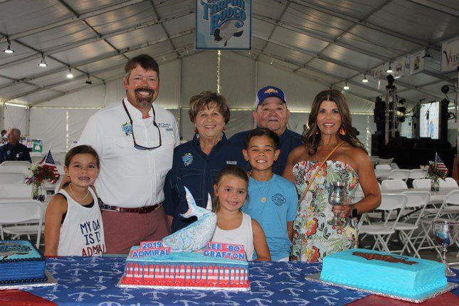 A family is posing for a picture in front of a cake.