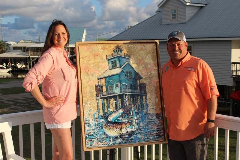 A man and a woman are standing next to each other holding a painting of a lighthouse.