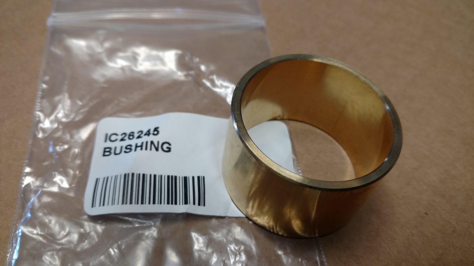 Brass bushing beside a labeled plastic bag on a cardboard surface.