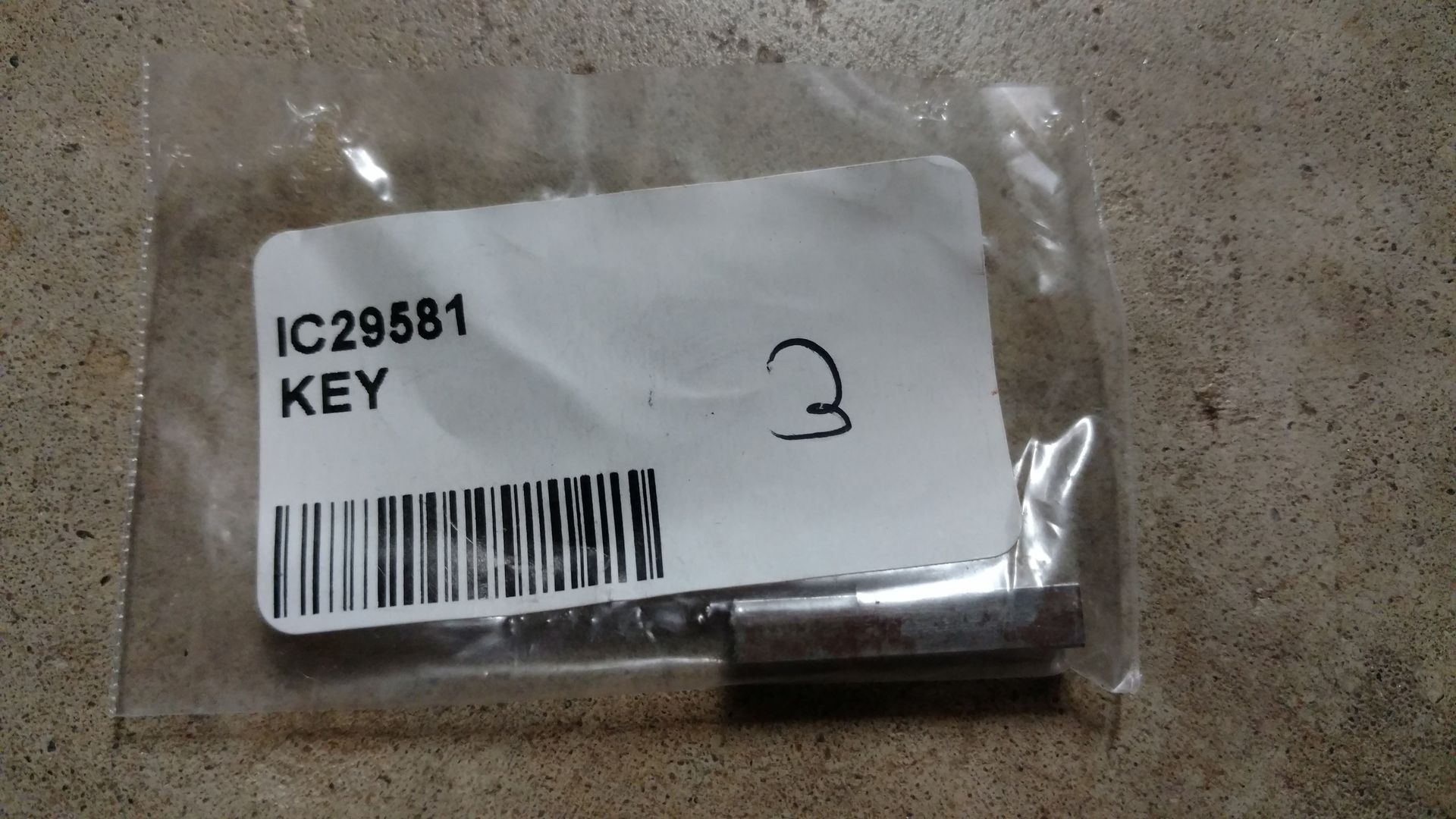 Clear plastic bag labeled “IC29581 KEY” on a concrete floor, with a barcode and handwritten 3.