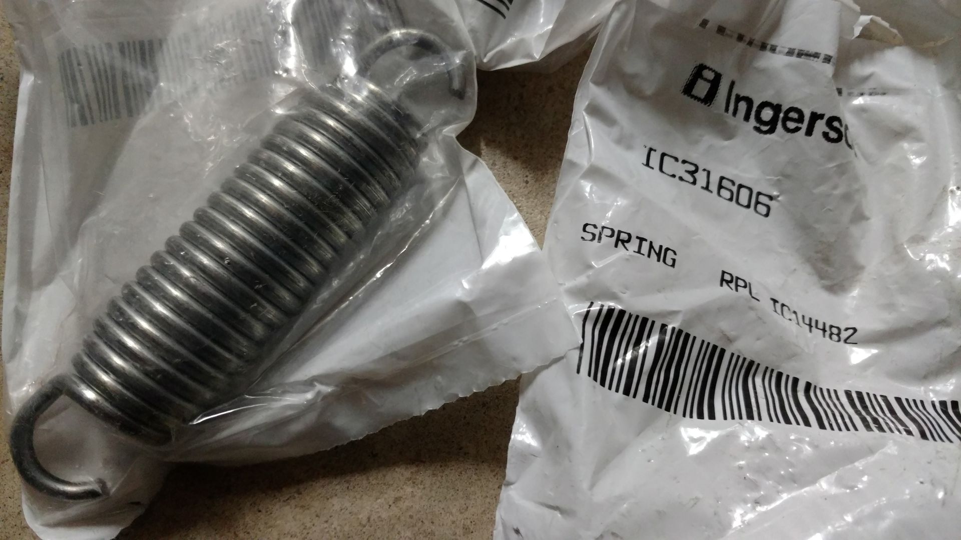 Close-up of a metal spring hook in a plastic bag beside a labeled parts package.