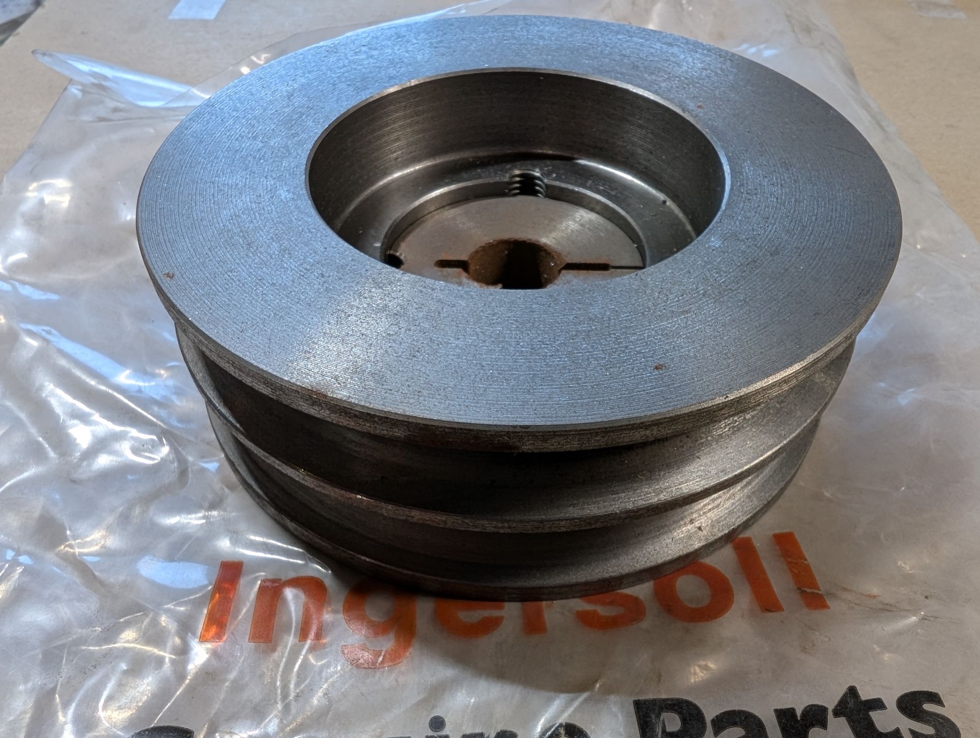 Gray metal pulley wheel with a grooved outer rim on a clear plastic bag