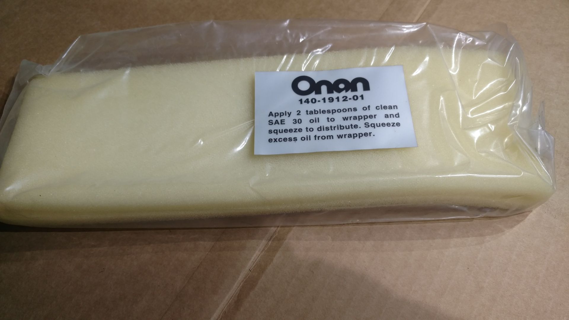 Wrapped beige Onan replacement part in clear plastic packaging on a cardboard surface