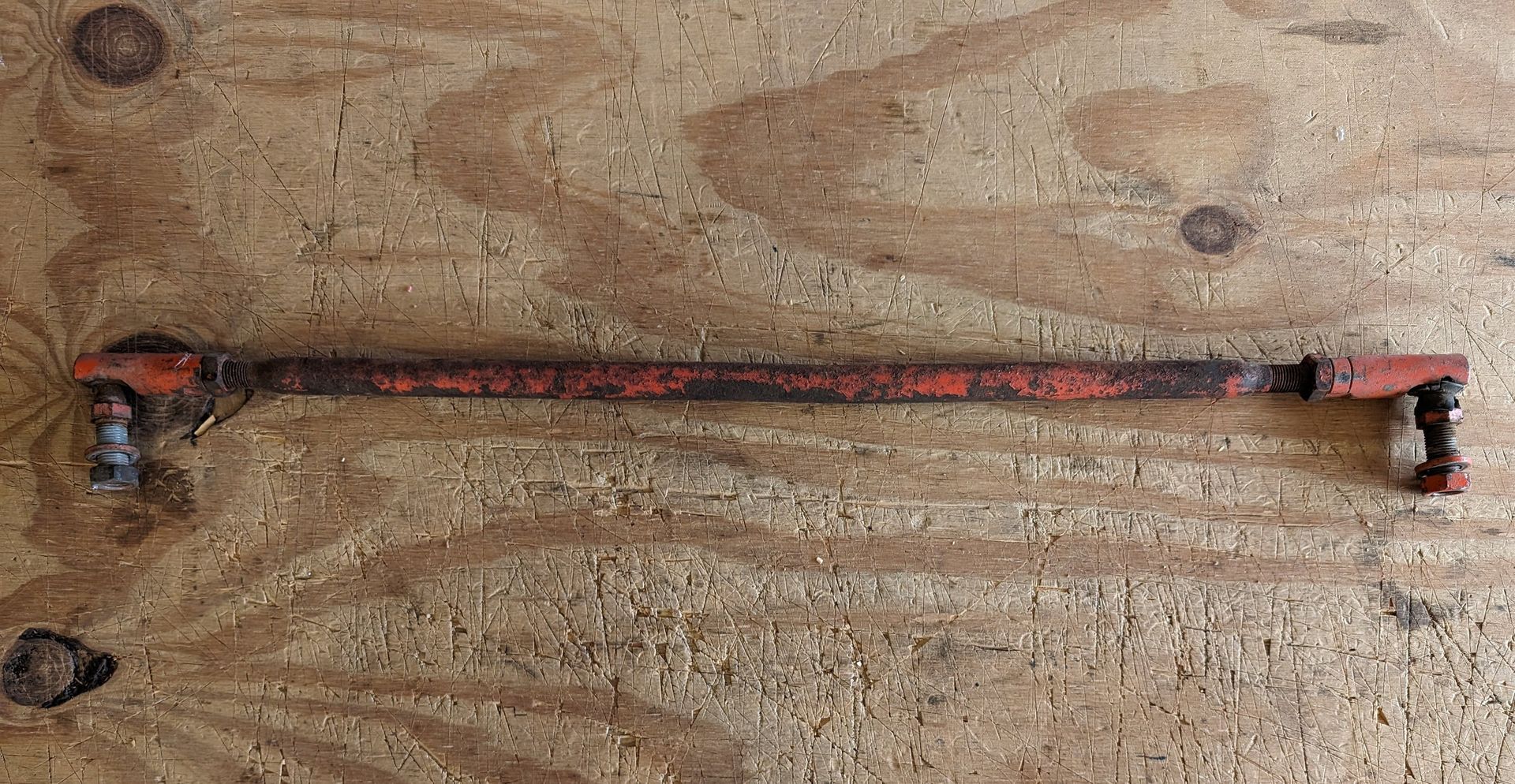 Rusty metal pipe with black fittings lying horizontally on sandy ground