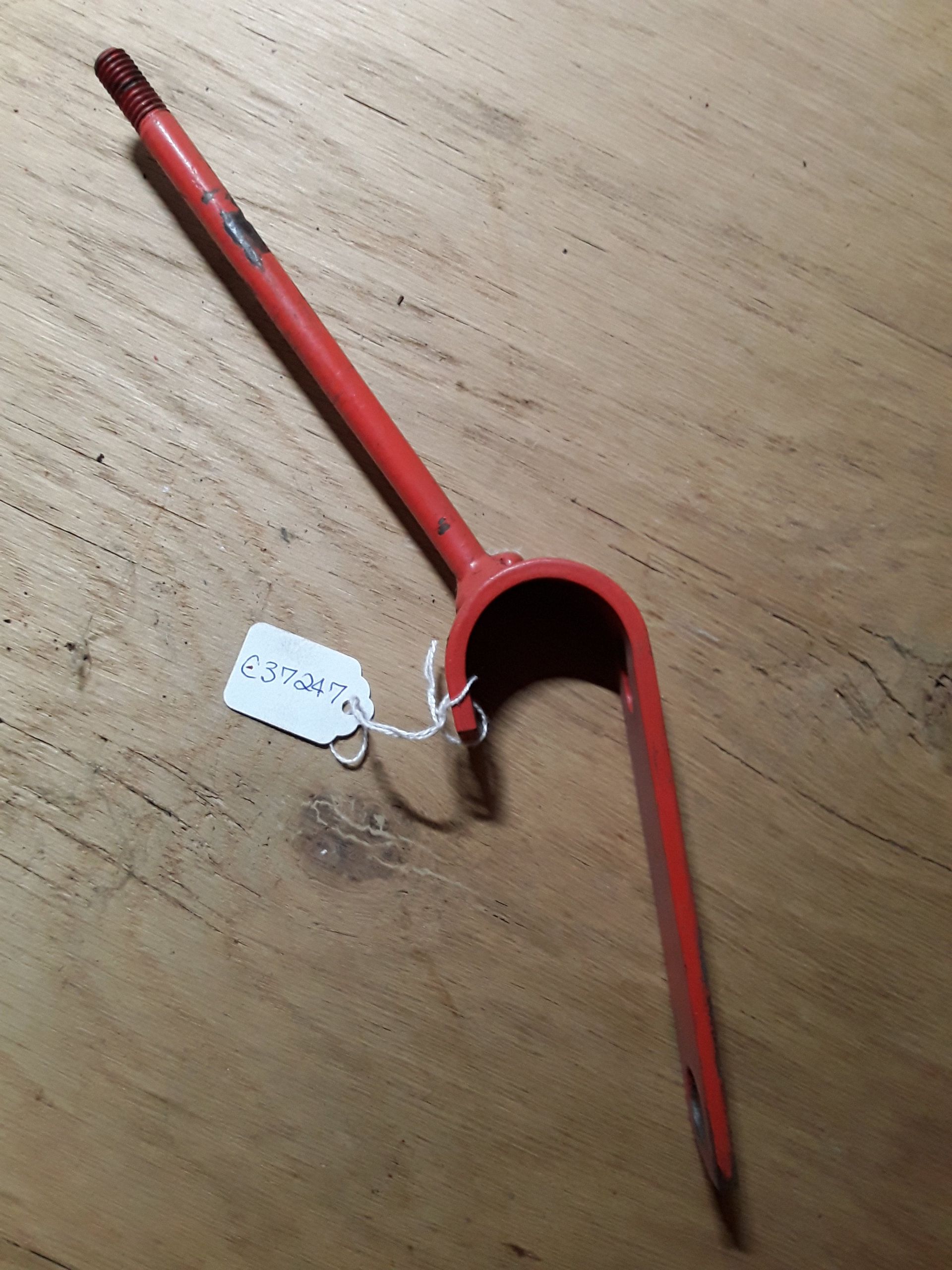 Red metal cane with a curved handle and white tag lying on a wooden floor.