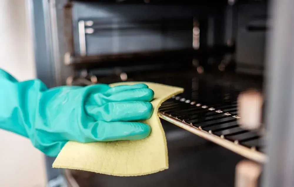 Person Wearing Green Glove Wiping Oven Rack With a Yellow Cloth Inside an Oven — Jamac Cleaning Services in Toronto, NSW