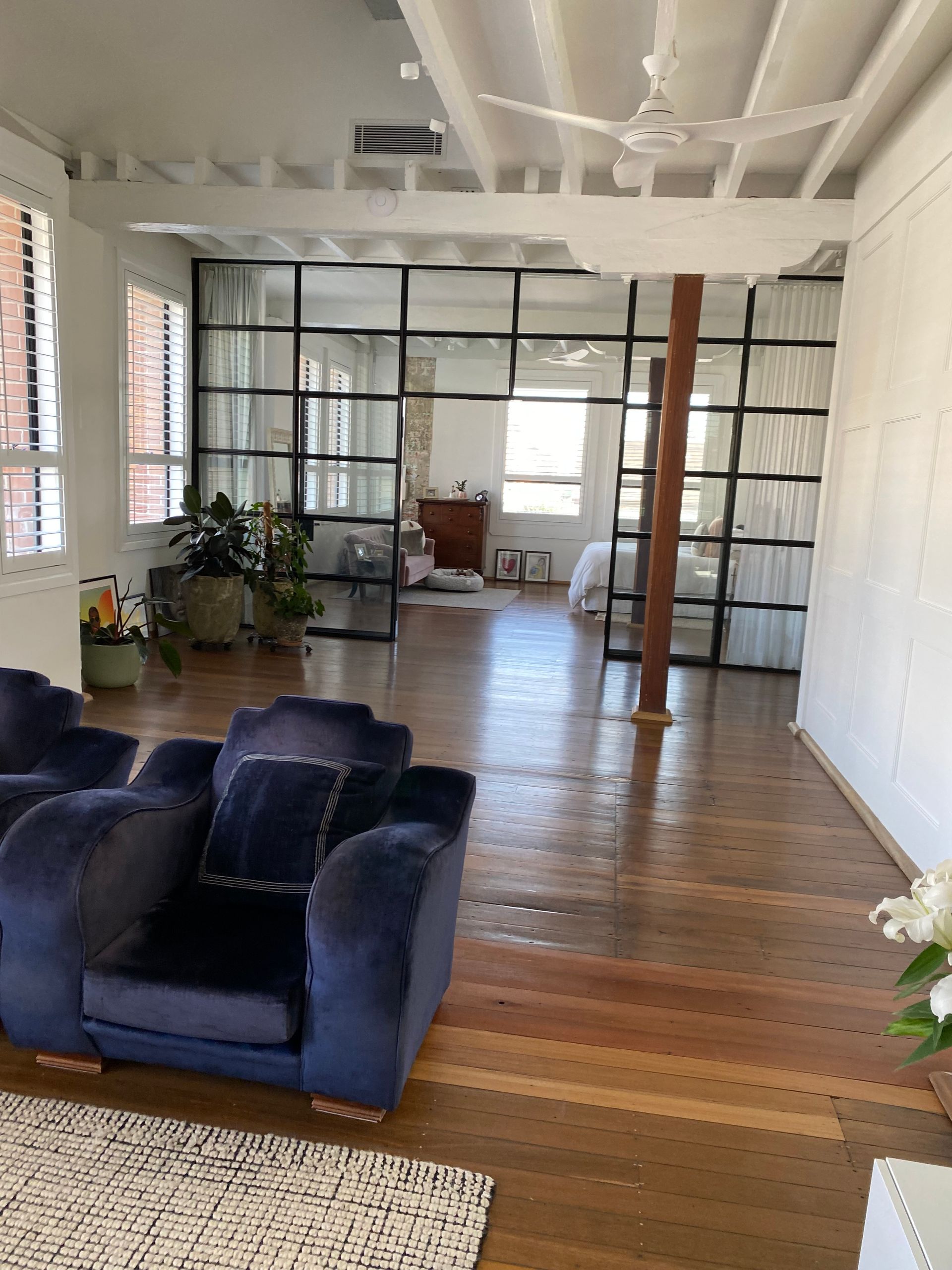 Bright loft living room with navy sofas, wood floors, and a glass wall at the far end