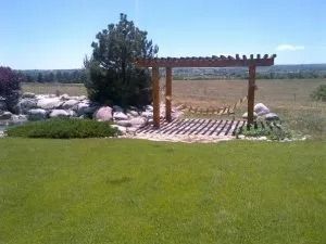 A wooden pergola is sitting in the middle of a lush green field.