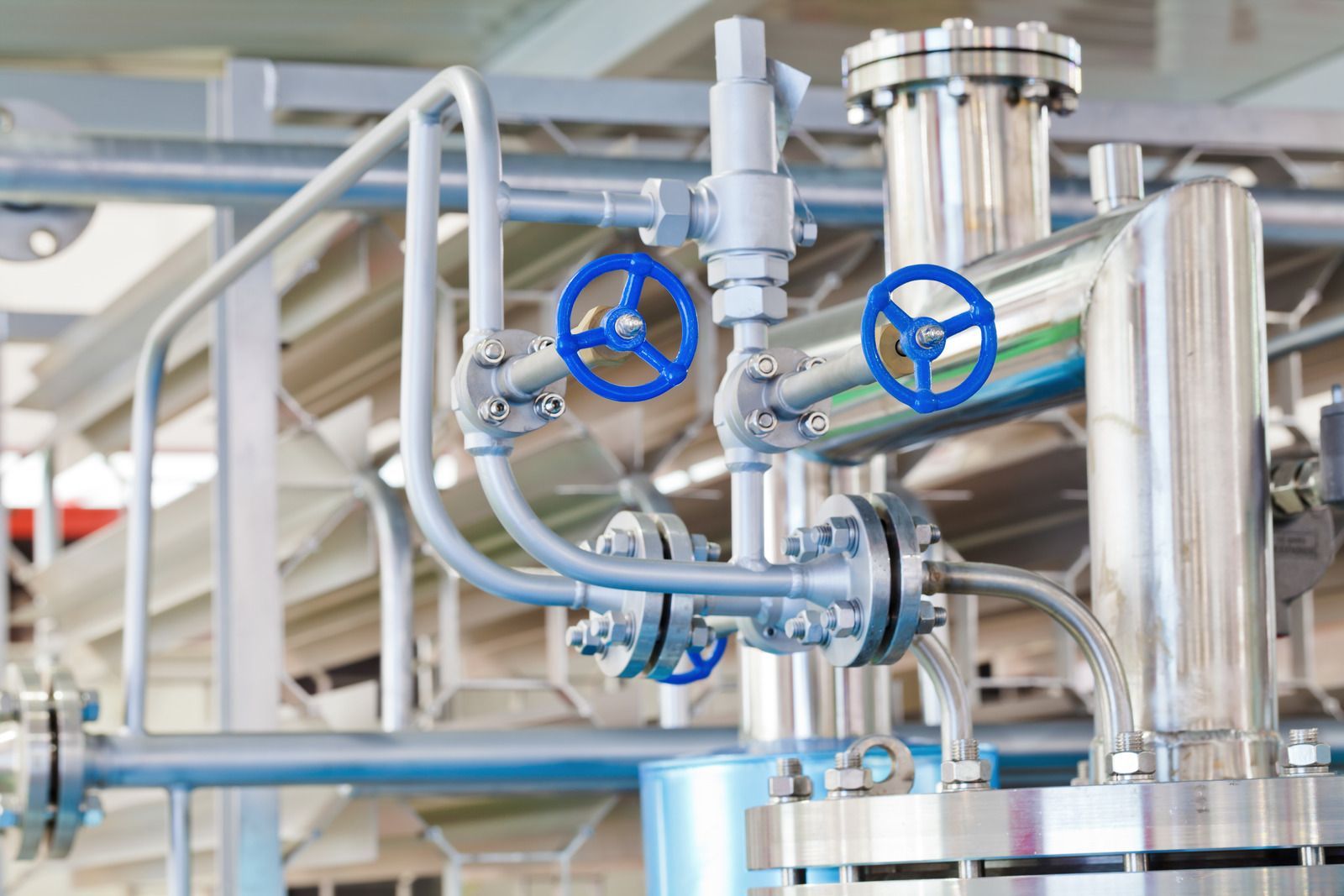 Industrial pipes and valves, blue handles, stainless steel construction.
