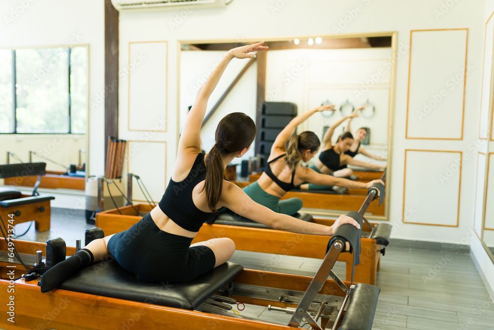 People stretching during a Pilates class. They're on reformer machines in a studio with a mirror.