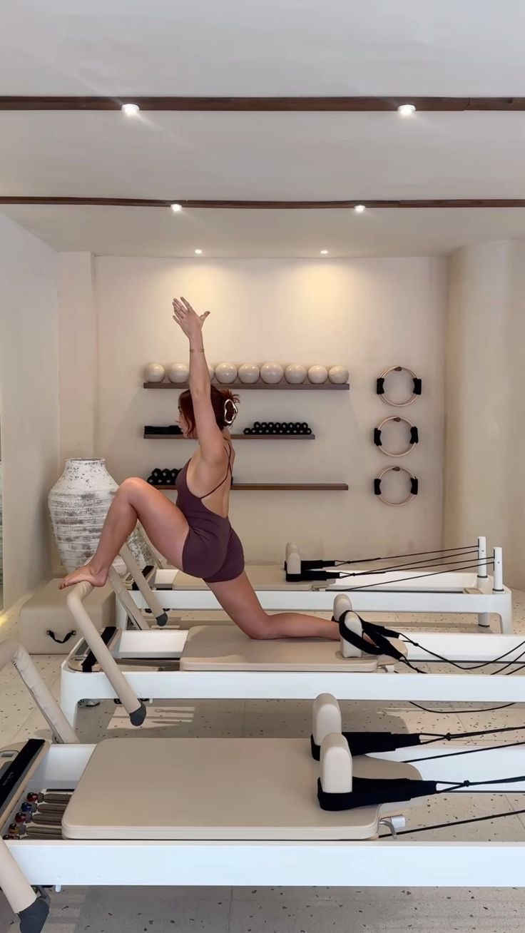 Person using a pilates reformer machine, leg extended with foot in a strap.
