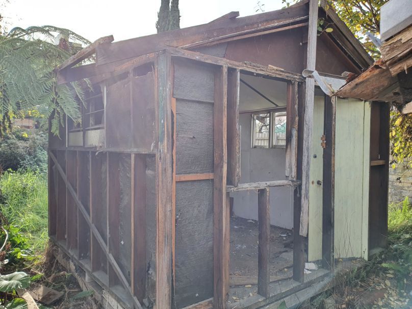 An old wooden shed is being demolished in a backyard.