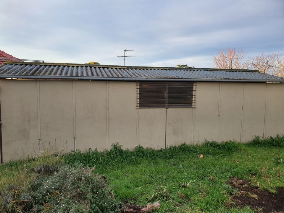 A shed with a window is sitting in the middle of a grassy field.