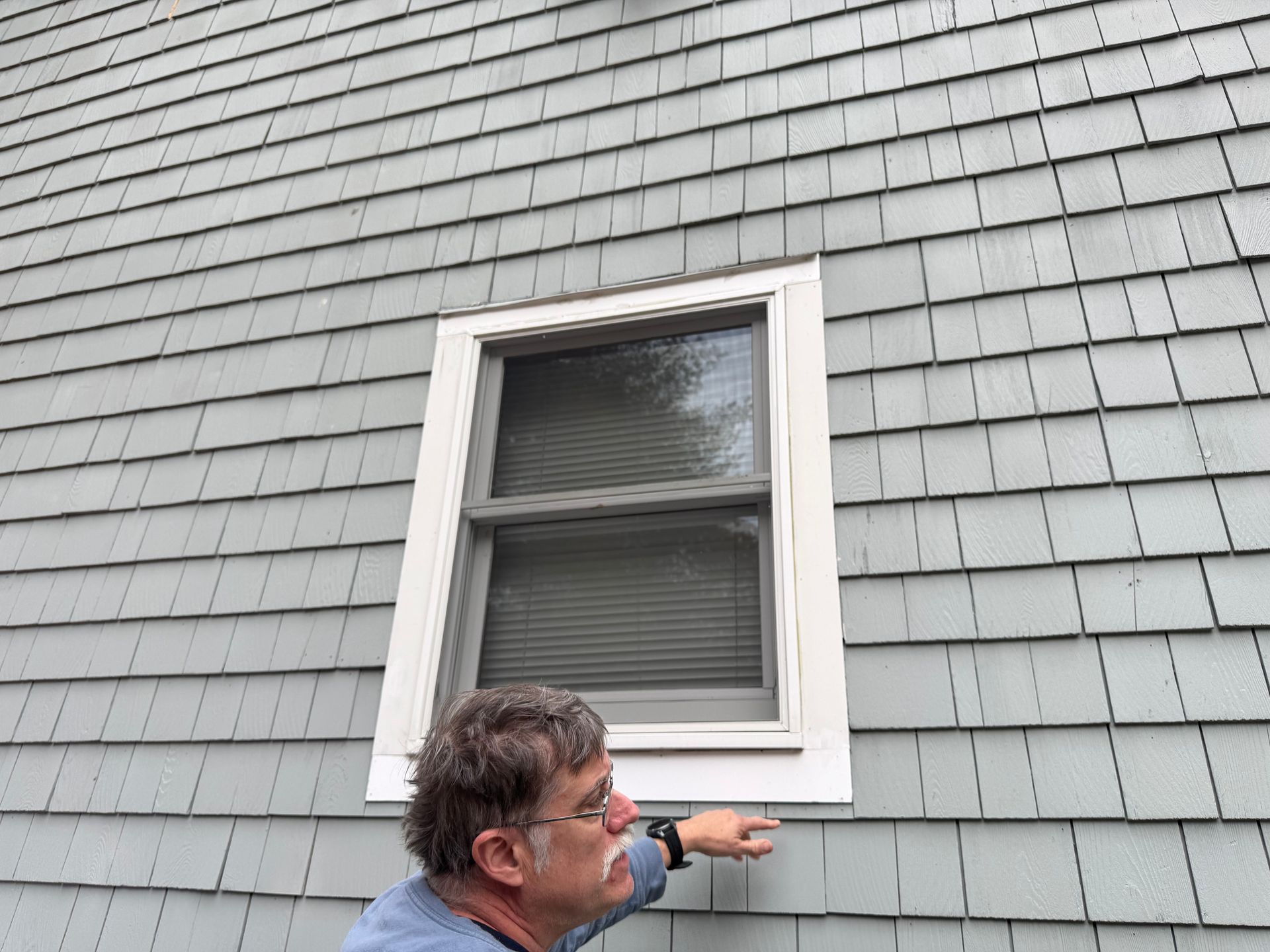 A man is pointing at a window on the side of a house.