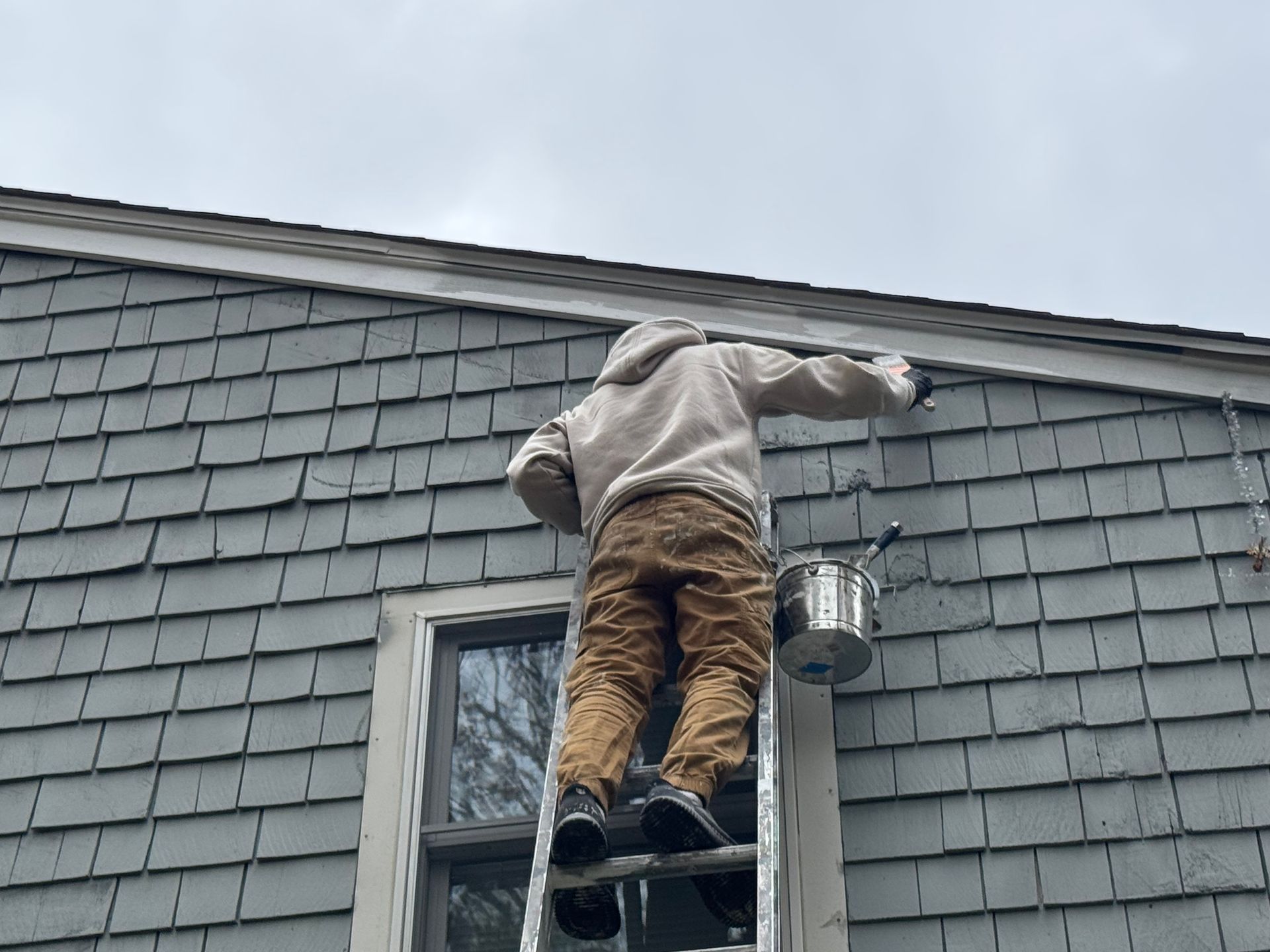 A man is standing on a ladder painting the side of a house.