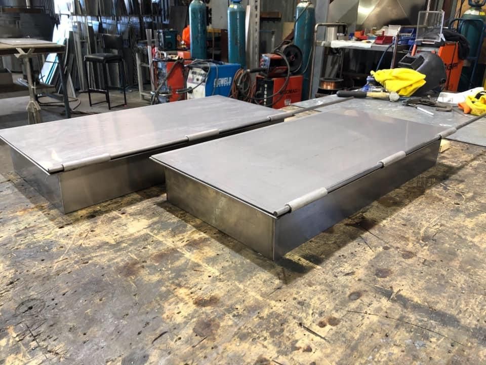 Two Stainless Steel Boxes Are Sitting on A Wooden Floor in A Factory — Shearwater Engineering in Gloucester, NSW