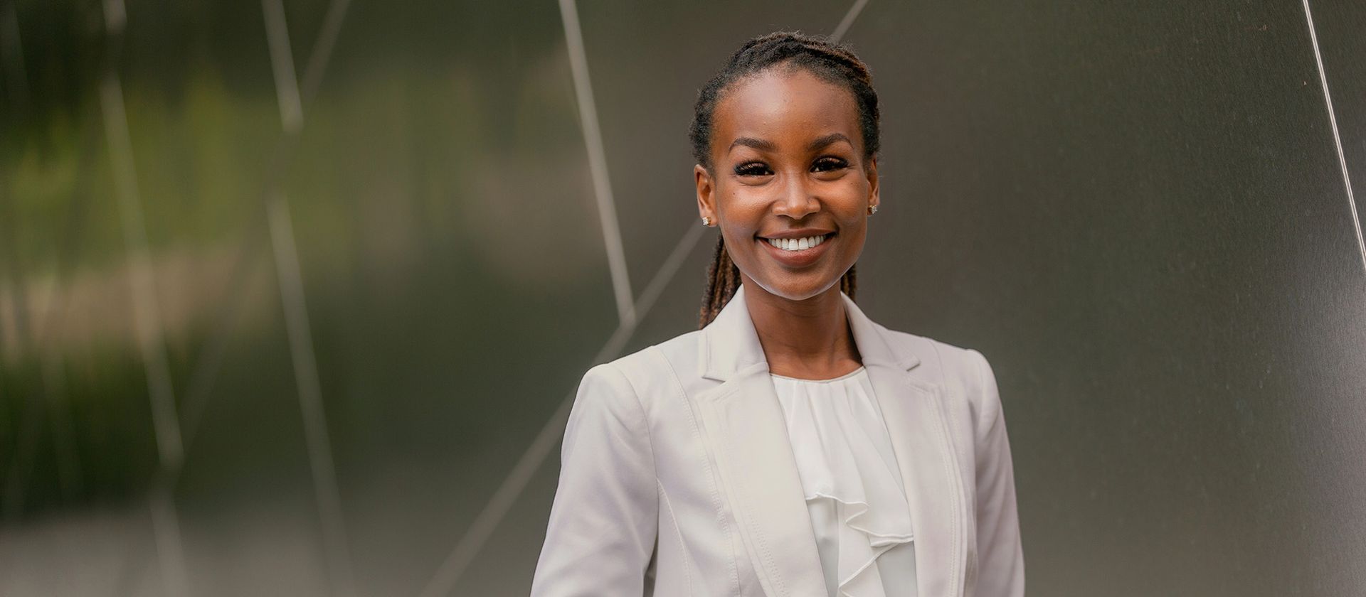 A woman in a white suit is smiling and standing in front of a glass wall.