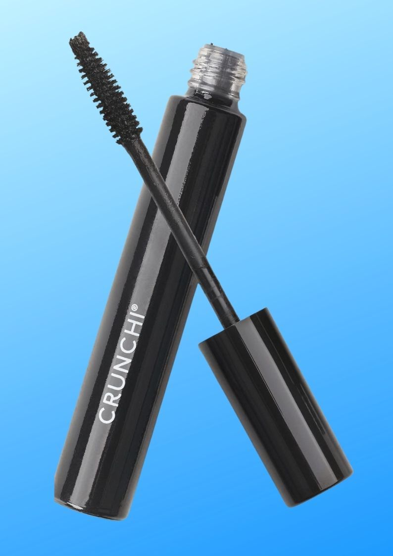 A person is holding a mascara brush with the words 